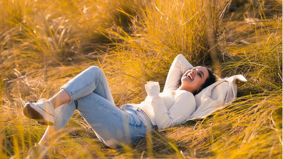 The grumpy sunshine romance trope by Vesta Romero. Girl laughing in hayfield wearing jeans and long white tee shirt